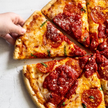 Kid reaching for a Pizza slice topped with Pepperoni and Crushed Tomatoes