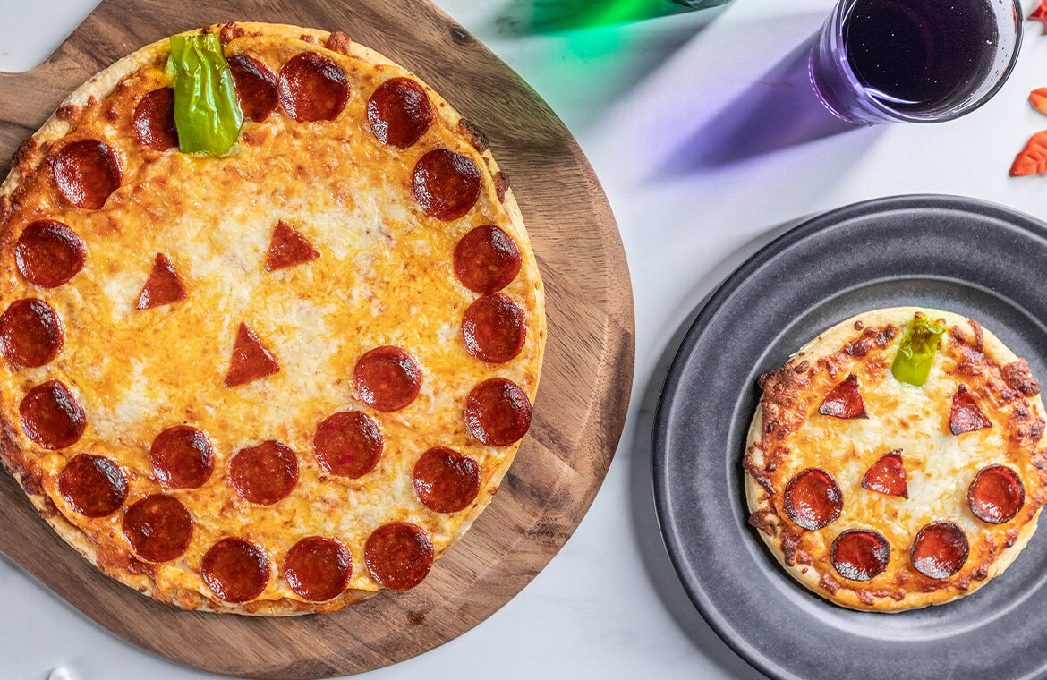 Pizza topped with pepperoni to resemble a jack-o-lantern face with a smaller one next to it