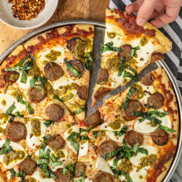 Pizza topped with meatballs, pesto, mozzarella and basil