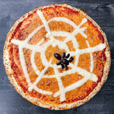 Pizza with toppings in the shape of a spider web with a spider