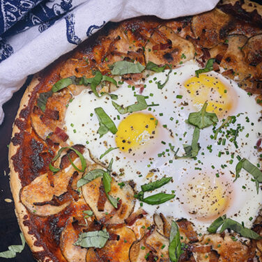 Pizza topped with potatoes, bacon and 3 sunny side up eggs