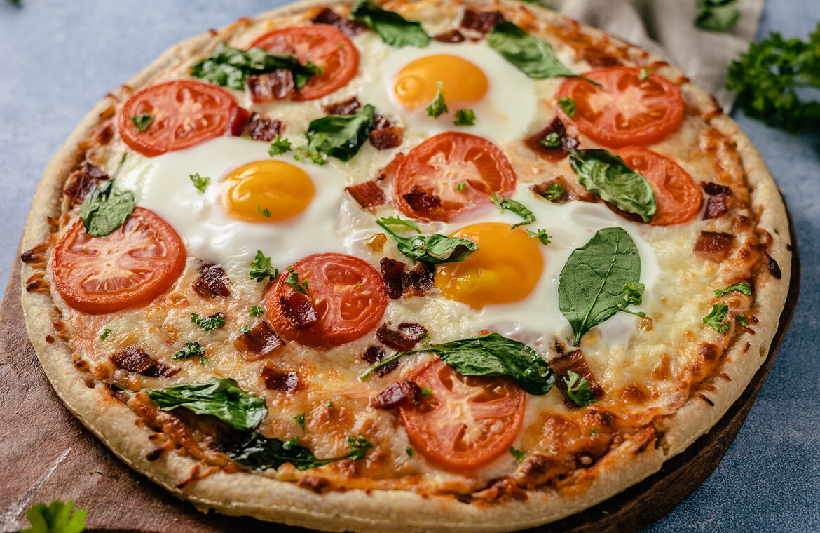 Pizza topped with eggs, tomato, bacon, and more
