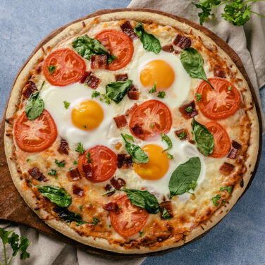 Pizza topped with eggs, tomato, bacon, and more