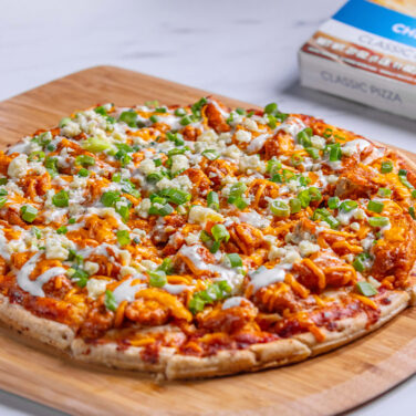Pizza topped with chicken, green onions, buffalo sauce, and more
