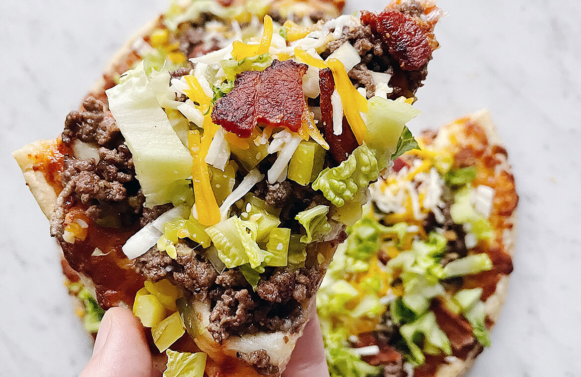 Pizza topped with ground beef, lettuce, bacon, cheese, and more ingredients