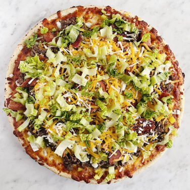 Pizza topped with ground beef, lettuce, bacon, cheese, and more ingredients