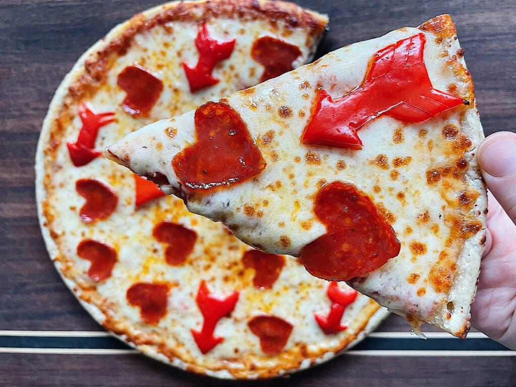Pizza topped with mini heart shaped pepperonis and bell peppers shaped as arrows