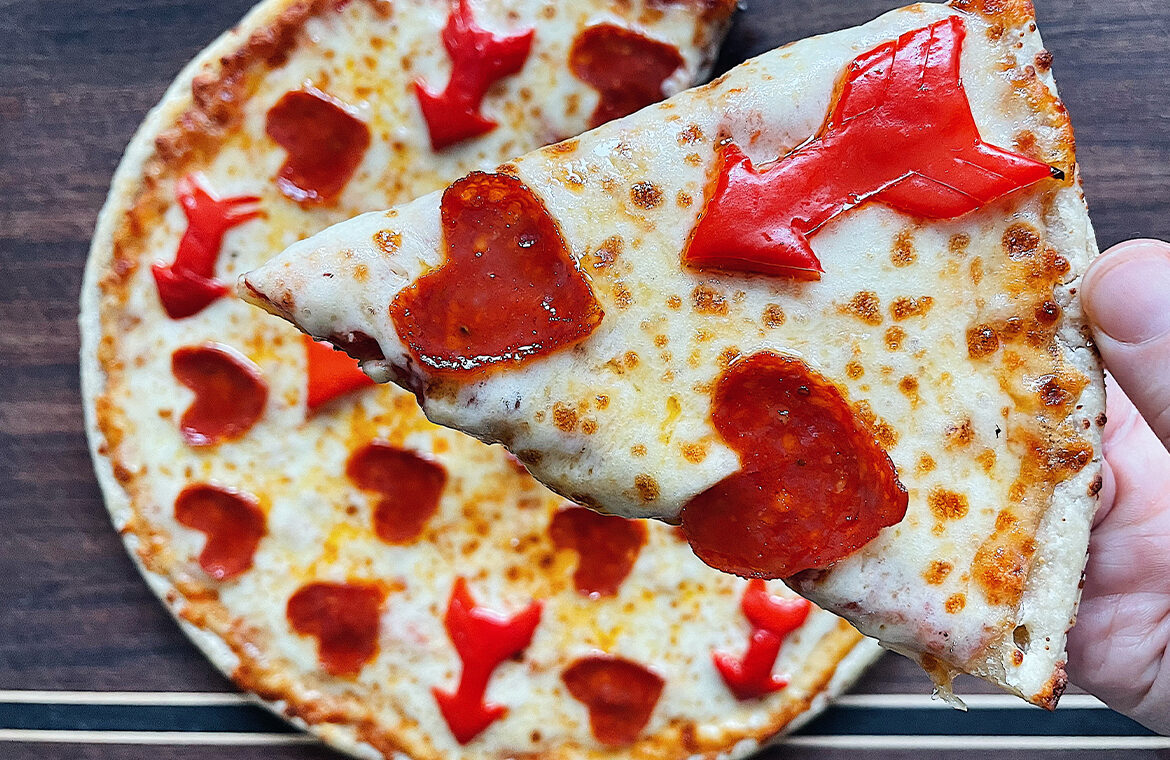 Pizza topped with mini heart shaped pepperonis and bell peppers shaped as arrows