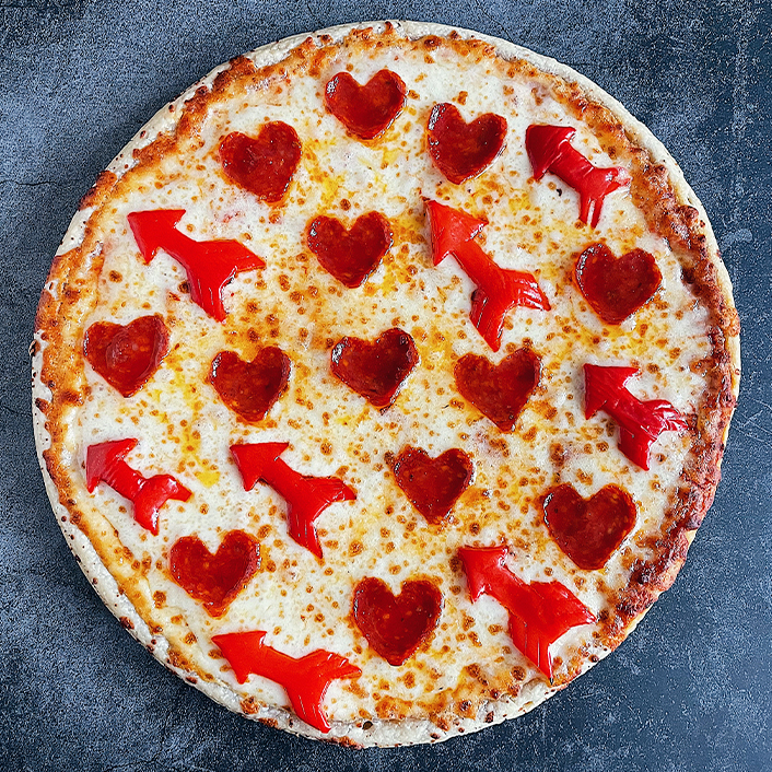 Pizza topped with mini heart shaped pepperonis and bell peppers shaped as arrows