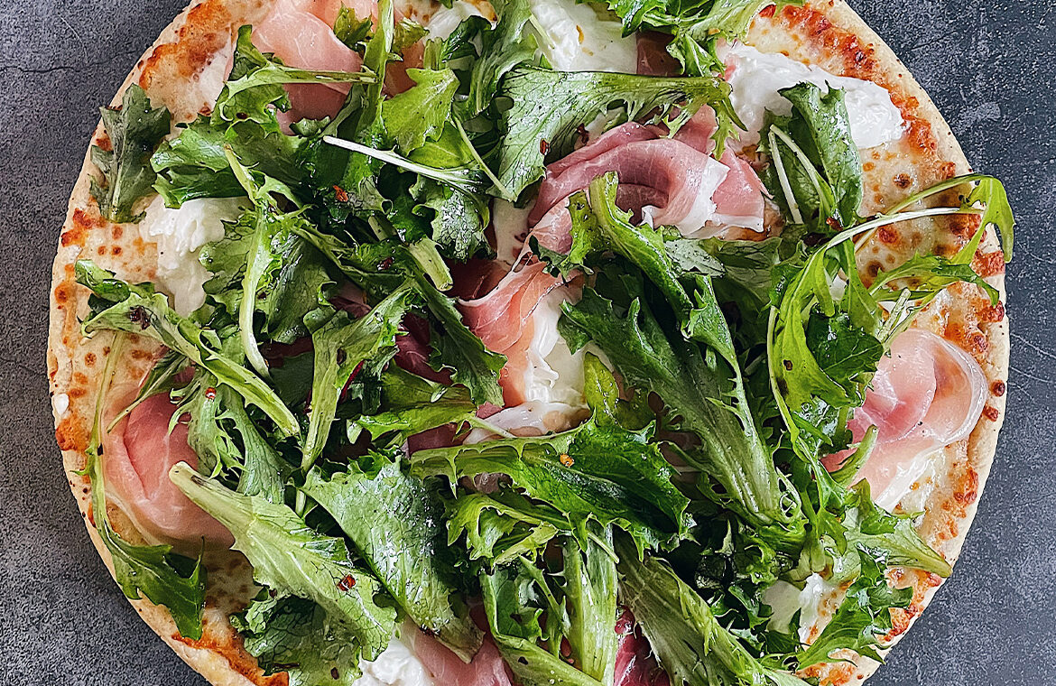 Pizza topped with baby greens, prosciutto, and burrata cheese