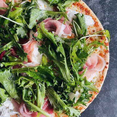 Pizza topped with baby greens, prosciutto, and burrata cheese