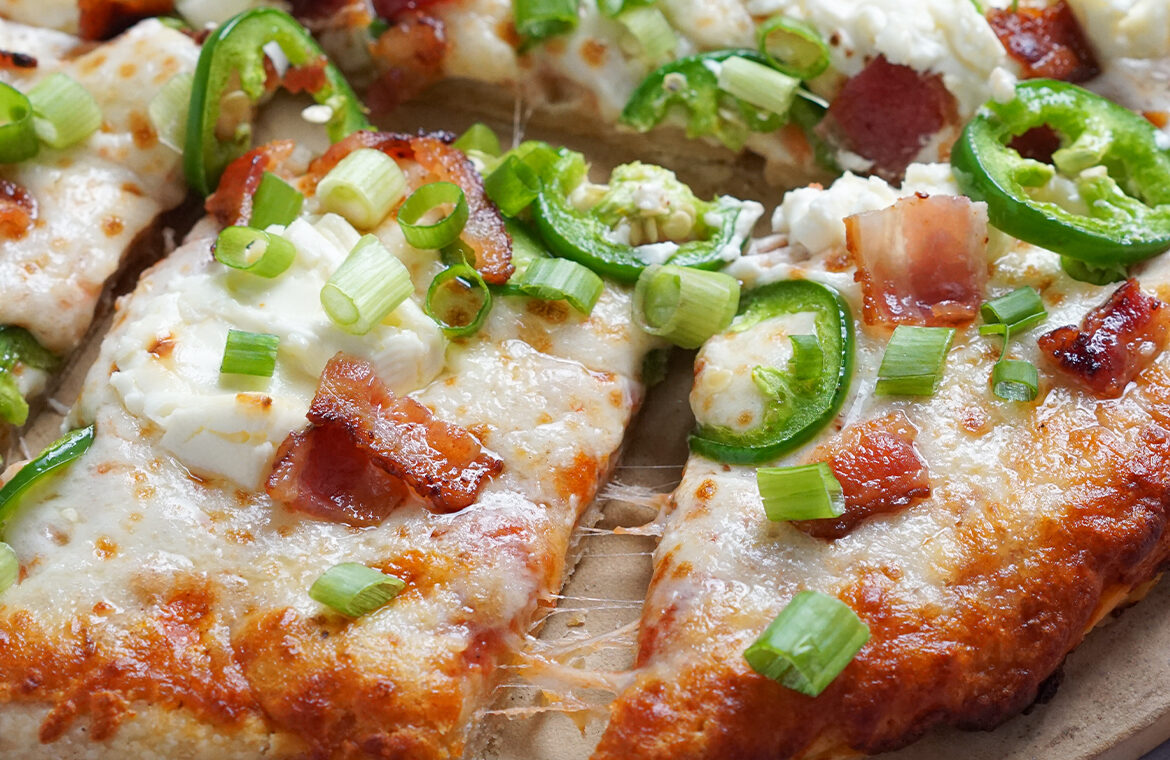 Pizza topped with bacon, ceam cheese, green onion, and jalapeno