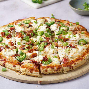 Pizza topped with bacon, ceam cheese, green onion, and jalapeno