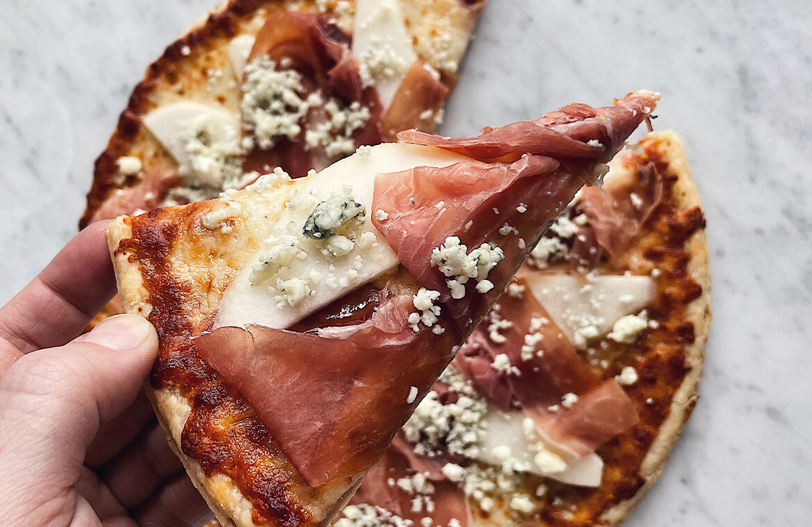 Pizza topped with sliced pears, prosciutto, and crumbled cheese