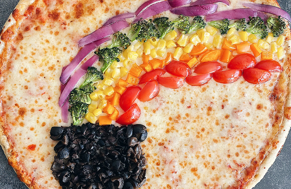 Pizza with topping in the shape of a rainbow leading to a pot of gold