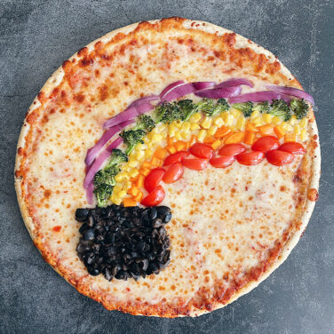 Pizza with topping in the shape of a rainbow leading to a pot of gold