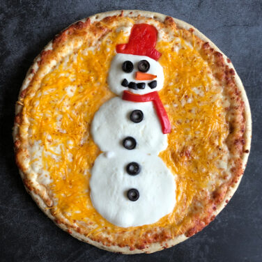 Pizza decorated with toppings in the shape of a snowman