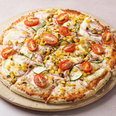 Pizza topped with corn, tomatoes, onion, and more