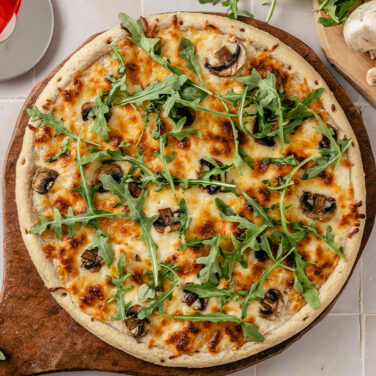 Pizza crust topped with white sauce, cheese, greens, and more