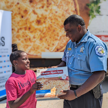 Chicago police officer handing a young girl a Home Run Inn pizza