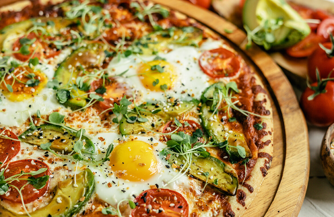Pizza topped with eggs, tomatoes, avocado, and more