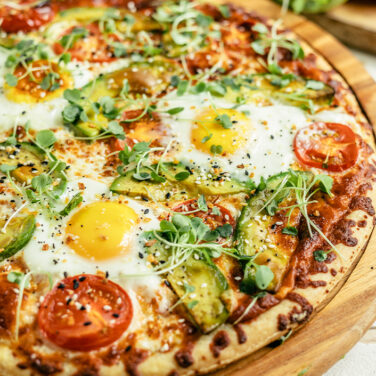 Pizza topped with eggs, tomatoes, avocado, and more