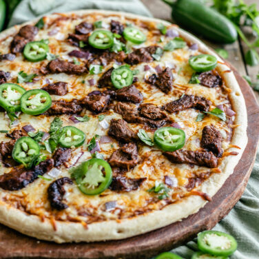 Pizza crust topped with Birria sauce, meat, jalapeños, and more
