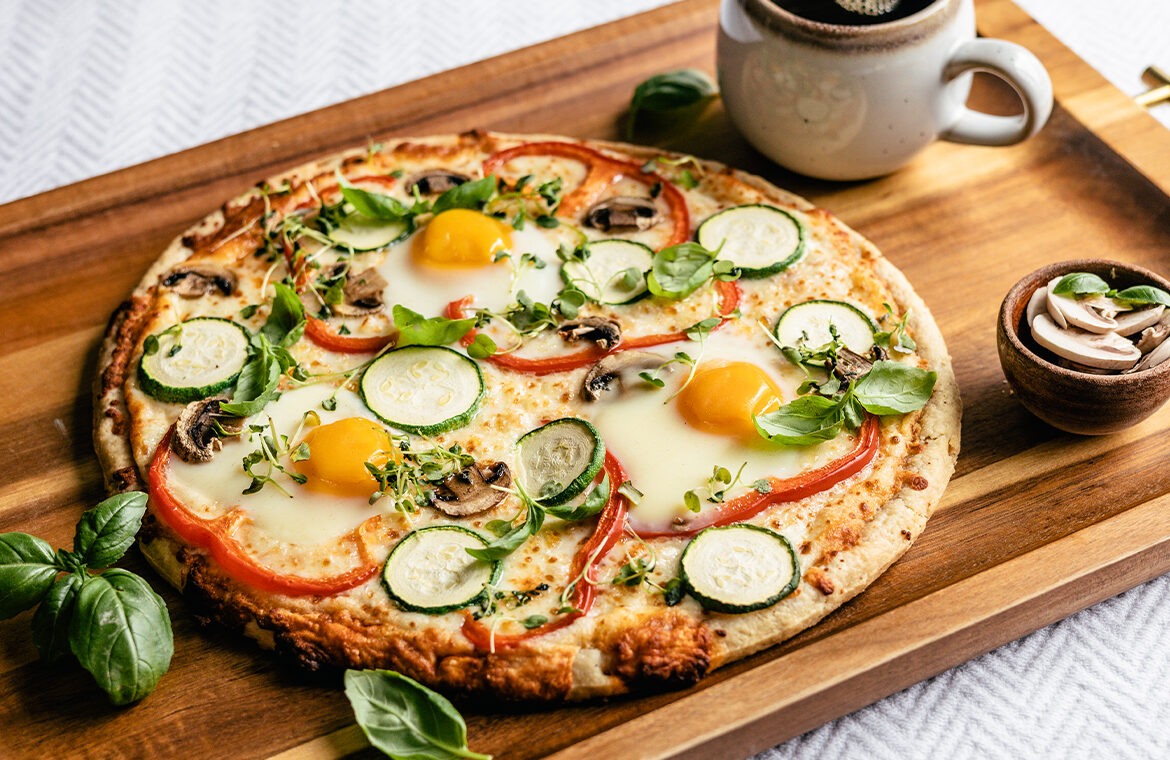 pizza on a tray in bed topped with eggs and veggies