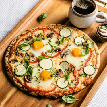 pizza on a tray in bed topped with eggs and veggies