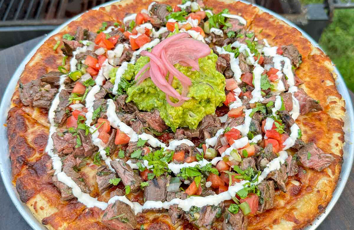 pizza topped with marinated steak, guacamole, salsa, and more