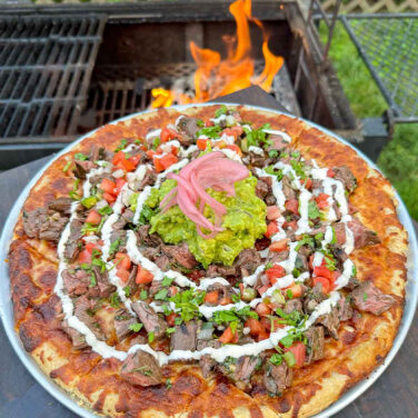 pizza topped with marinated steak, guacamole, salsa, and more