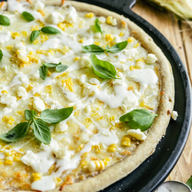 Cooked pizza crust topped with corn, ranch an more