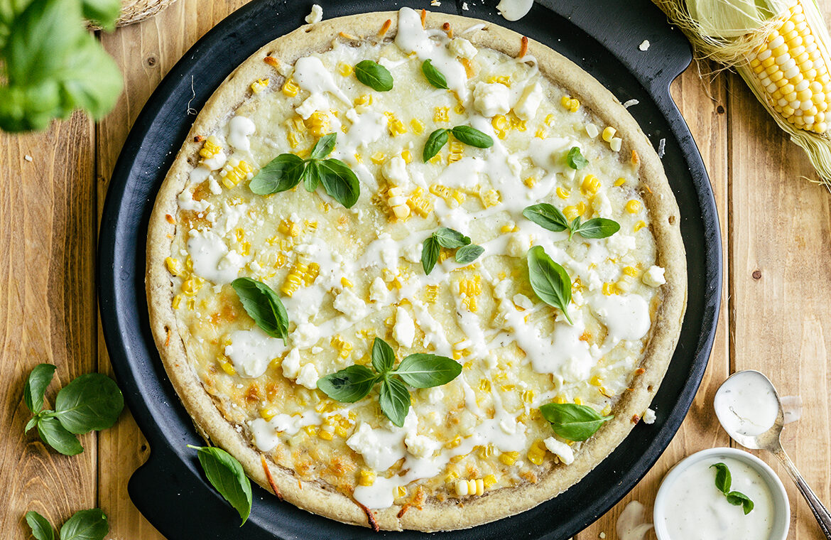 Cooked pizza crust topped with corn, ranch an more
