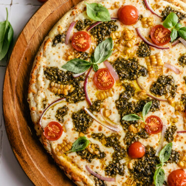 grilled pizza topped with tomatoes, pesto, onion, and more