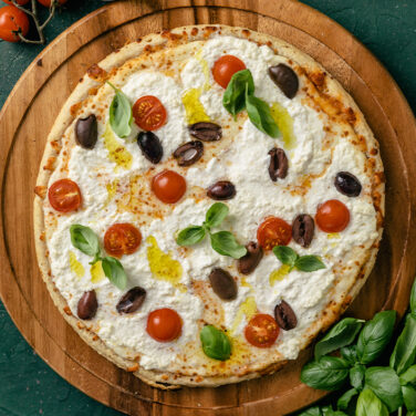 pizza topped with olives, tomatoes, olive oil, basil, and more