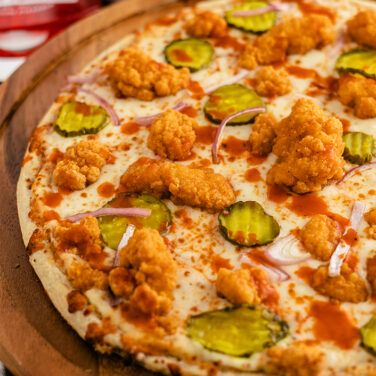 pizza topped with popcorn chicken, buffalo sauce, and pickles