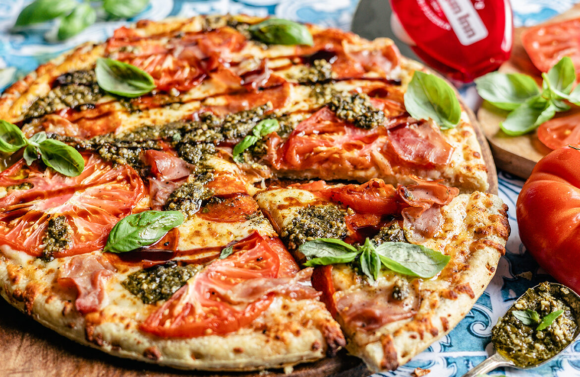 Pizza topped with tomato, pesto, fresh basil, and balsamic glaze