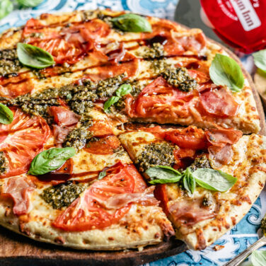 Pizza topped with tomato, pesto, fresh basil, and balsamic glaze