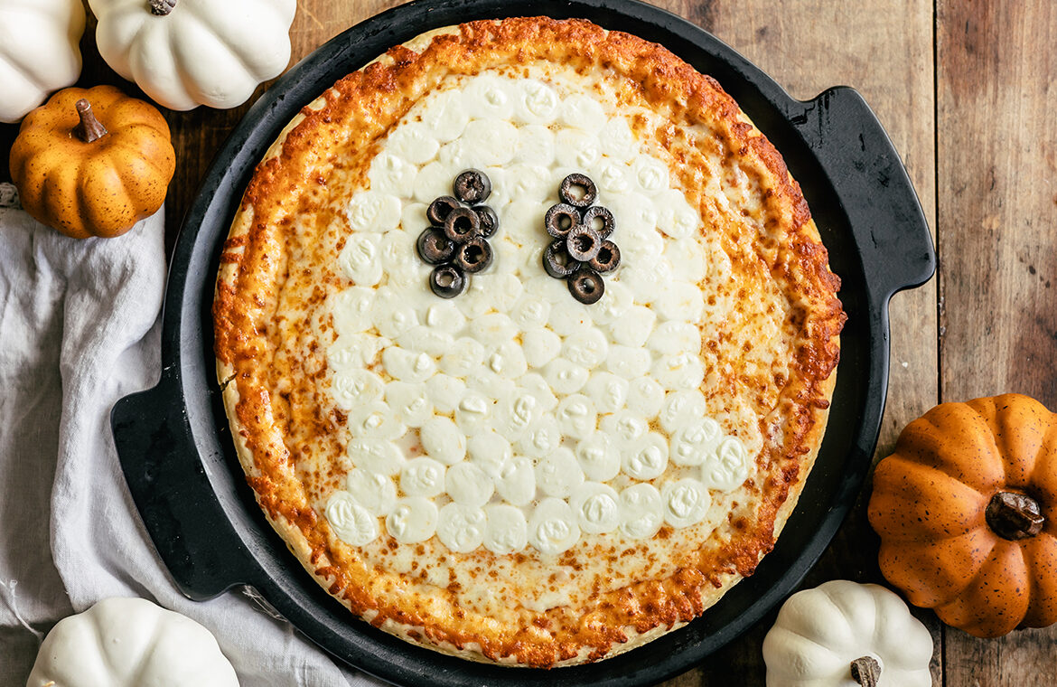 Baked pizza with mozzarella balls in the shape of a ghost with olives as eyes