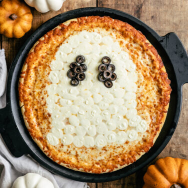 Baked pizza with mozzarella balls in the shape of a ghost with olives as eyes