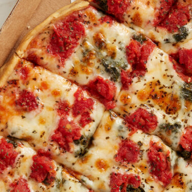 Pizza with tomatoes and spinach sitting in to go cardboard box