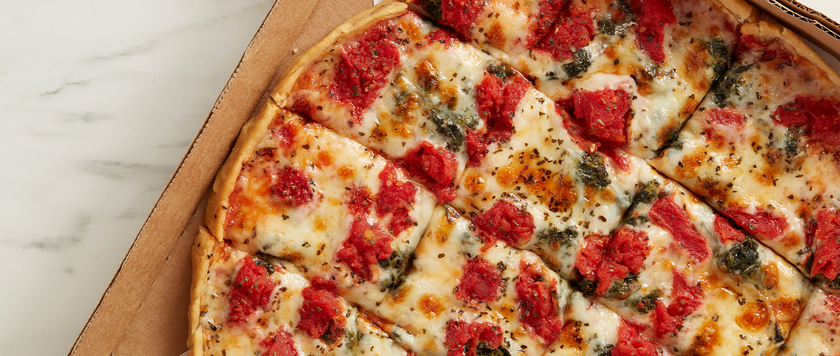 Pizza with tomatoes and spinach sitting in to go cardboard box