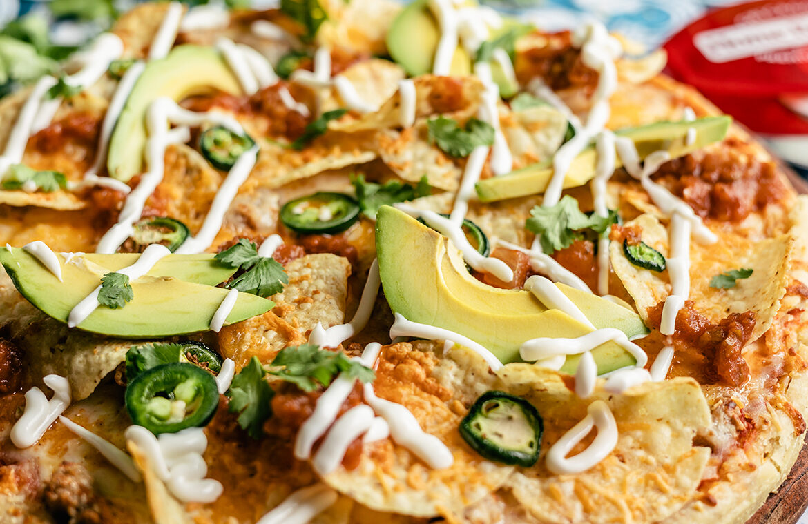 Pizza topped with chips, avocado, sour cream, jalapeños and more