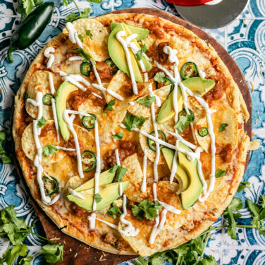 Pizza topped with chips, avocado, sour cream, jalapeños and more