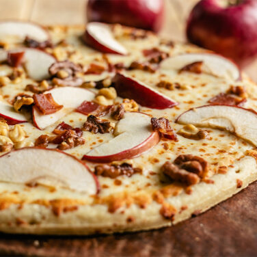 Pizza topped with apple slices, bacon, and walnuts