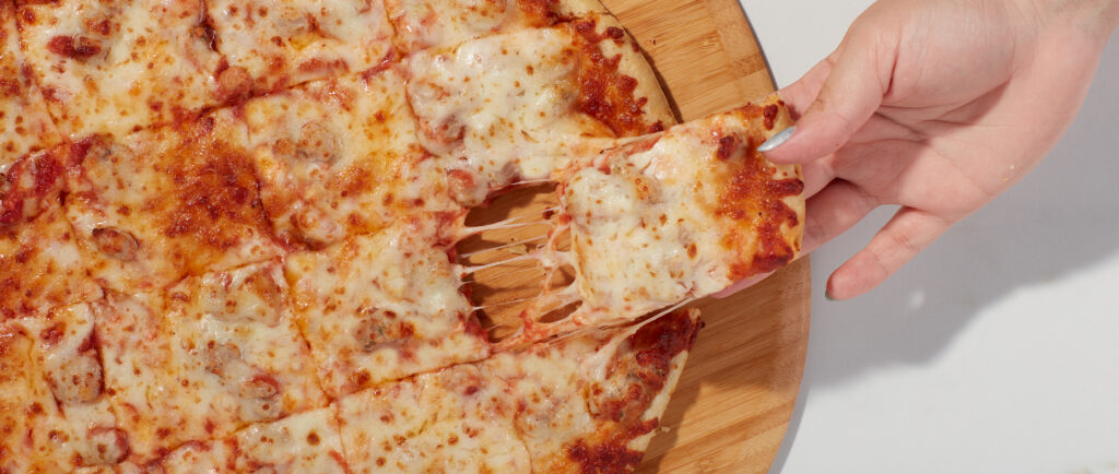 Sausage pizza slice being grabbed from a square-cut pizza