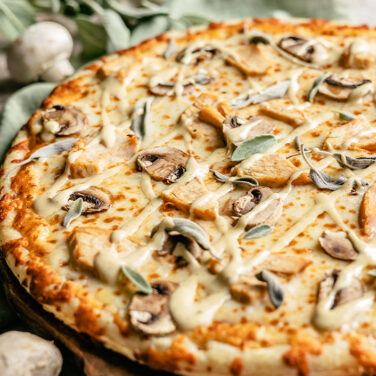 Cooked pizza topped with mushroom, chicken, sage, and garlic aioli