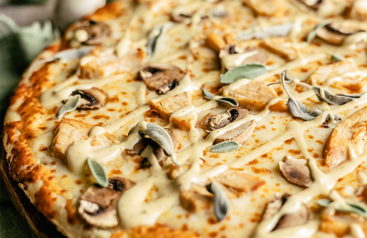 Cooked pizza topped with mushroom, chicken, sage, and garlic aioli