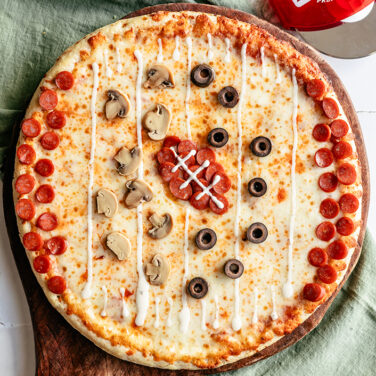 Pizza topped with mini pepperoni in the shape of a football, and black olives and mushrooms in play formation