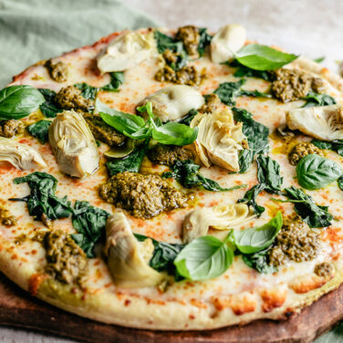 Pizza topped with spinach, artichoke, and pesto